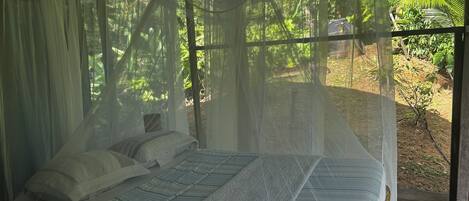 A bed with a canopy in a room with a view of greenery.