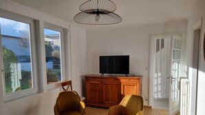 Una habitación con dos sillas, un televisor sobre un mueble de madera y un ventilador de techo.