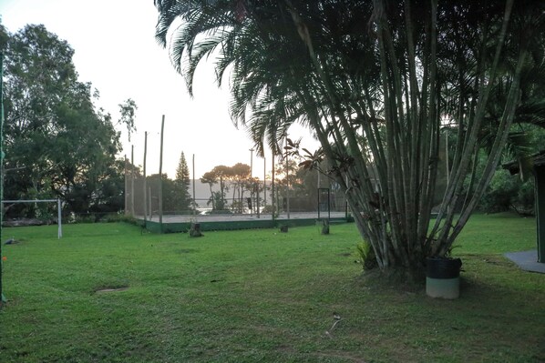 A grassy outdoor area with a large tree, a fence, and a structure in the background. - Praia Mole Hotel (Florianópolis)