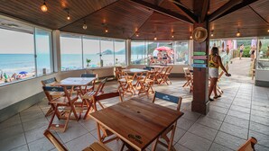 A restaurant with wooden tables and chairs, large windows overlooking the beach, and a sign indicating the direction to the beach. - Praia Mole Hotel (Florianópolis)
