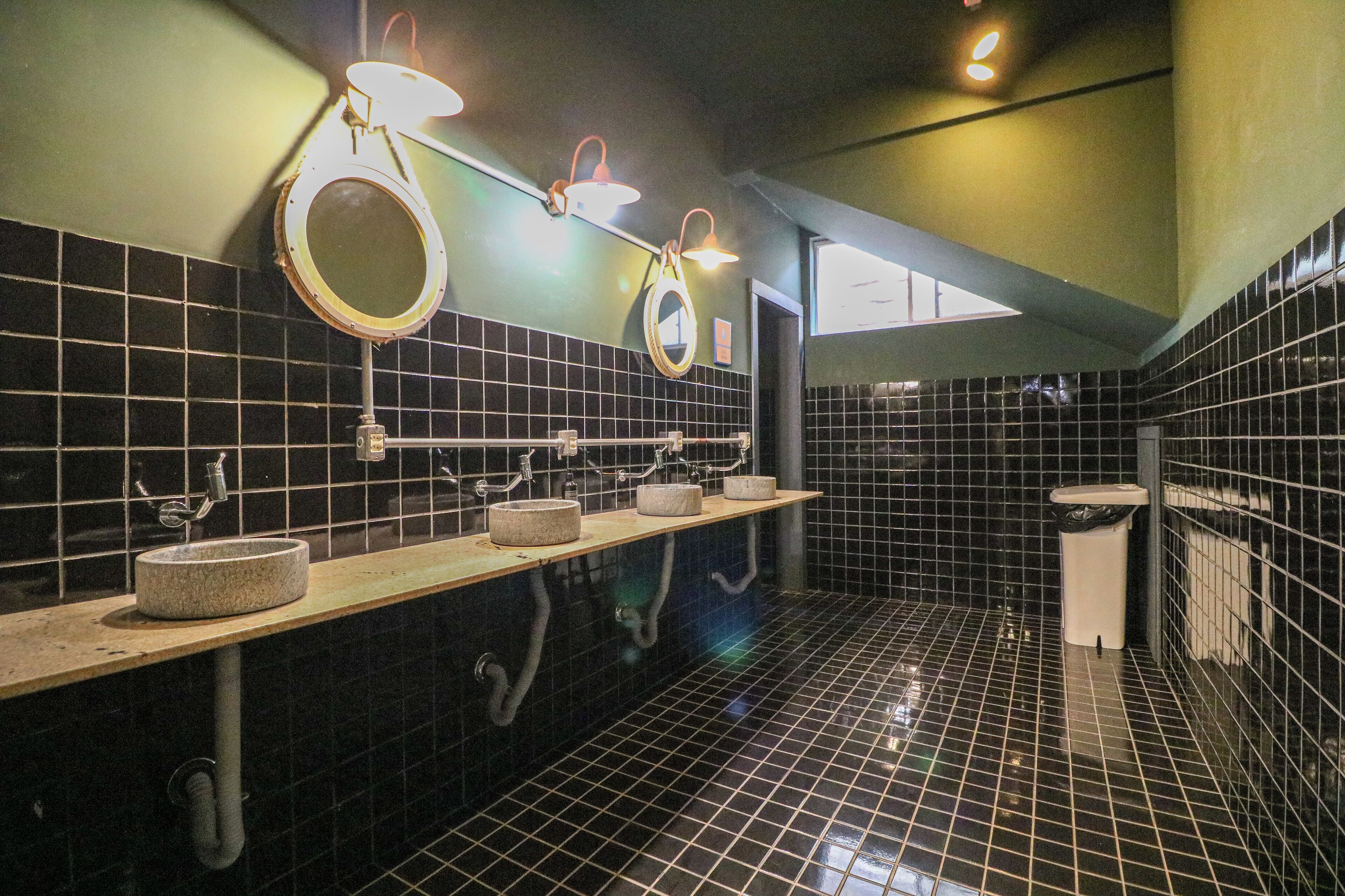 A public restroom with black tiled walls, three sinks with round basins, and overhead lighting.
