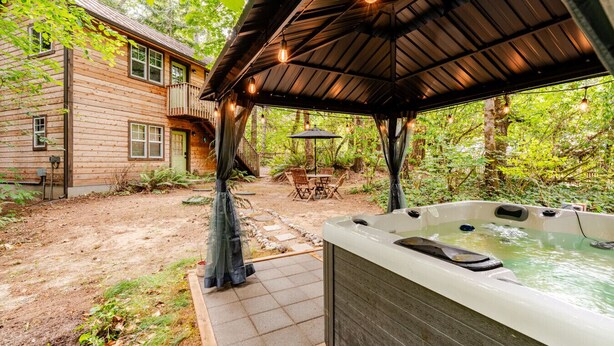A wooden cabin with a hot tub, outdoor seating, and a covered patio area. - Charming Creekside Studio Near Ferries to Seattle (Port Orchard)