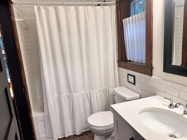 Un baño con cortina de ducha blanca, un inodoro y un lavamanos con espejo.