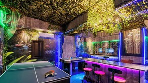 Una habitación con mesa de ping pong, zona de bar con taburetes y un mural de un paisaje urbano futurista.