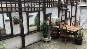 A wooden table with four chairs, potted plants, and a window with a view of a building. - Darlington Delight - Spacious 3 Bedroom House (Darlington)