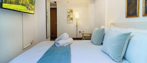 Quarto de hotel com uma cama, televisão na parede, mesa de cabeceira e abajur.