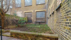 Un patio con pared de ladrillo, un árbol y una pequeña zona ajardinada.