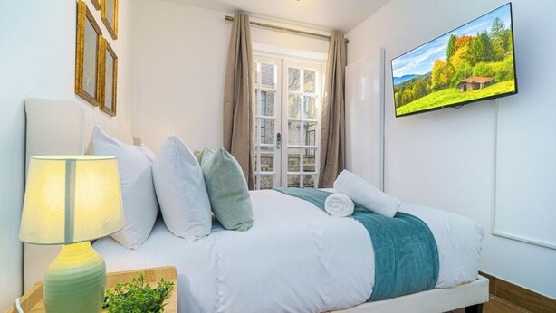 Un dormitorio con cama, televisión, lámpara y ventana con cortinas.