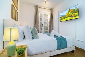 A bedroom with a bed, a TV, a lamp, and a window with curtains. - Angel x Kings Cross Rooms (London)