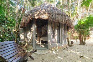 A thatched-roof hut with a bench outside, surrounded by greenery.