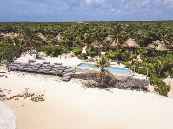 A resort with a pool, lounge area, and thatched-roof structures surrounded by palm trees.