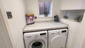 A laundry room with two Bosch washing machines, a window with a view of a brick building, and a shelf with decorative items. - Apartmentsleeps8-wifi-famillyfriendly-citycentre (Royal Tunbridge Wells)