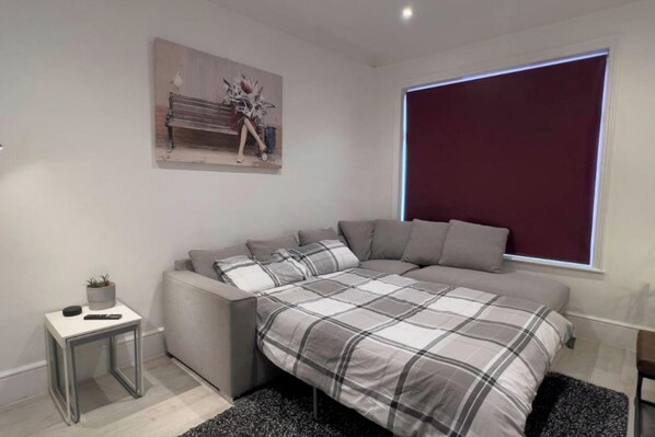 A modern bedroom with a bed, a small bedside table, a window with blinds, and a wall-mounted painting. - Apartmentsleeps8-wifi-famillyfriendly-citycentre (Royal Tunbridge Wells)