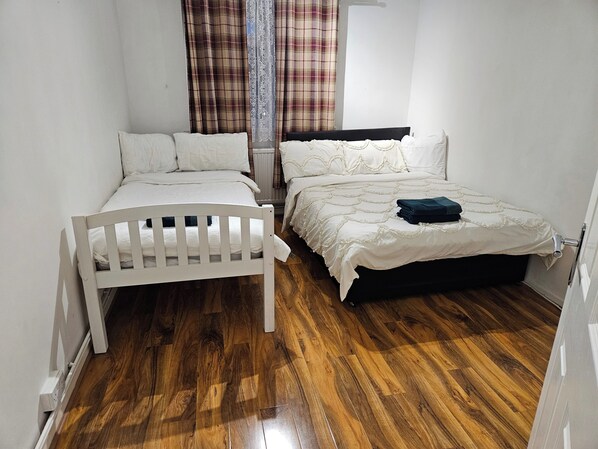 A small, clean room with two beds, wooden flooring, and plaid curtains. - Mitcham Junction - 2 Bed Apartment - Sleeps 6 (Mitcham)