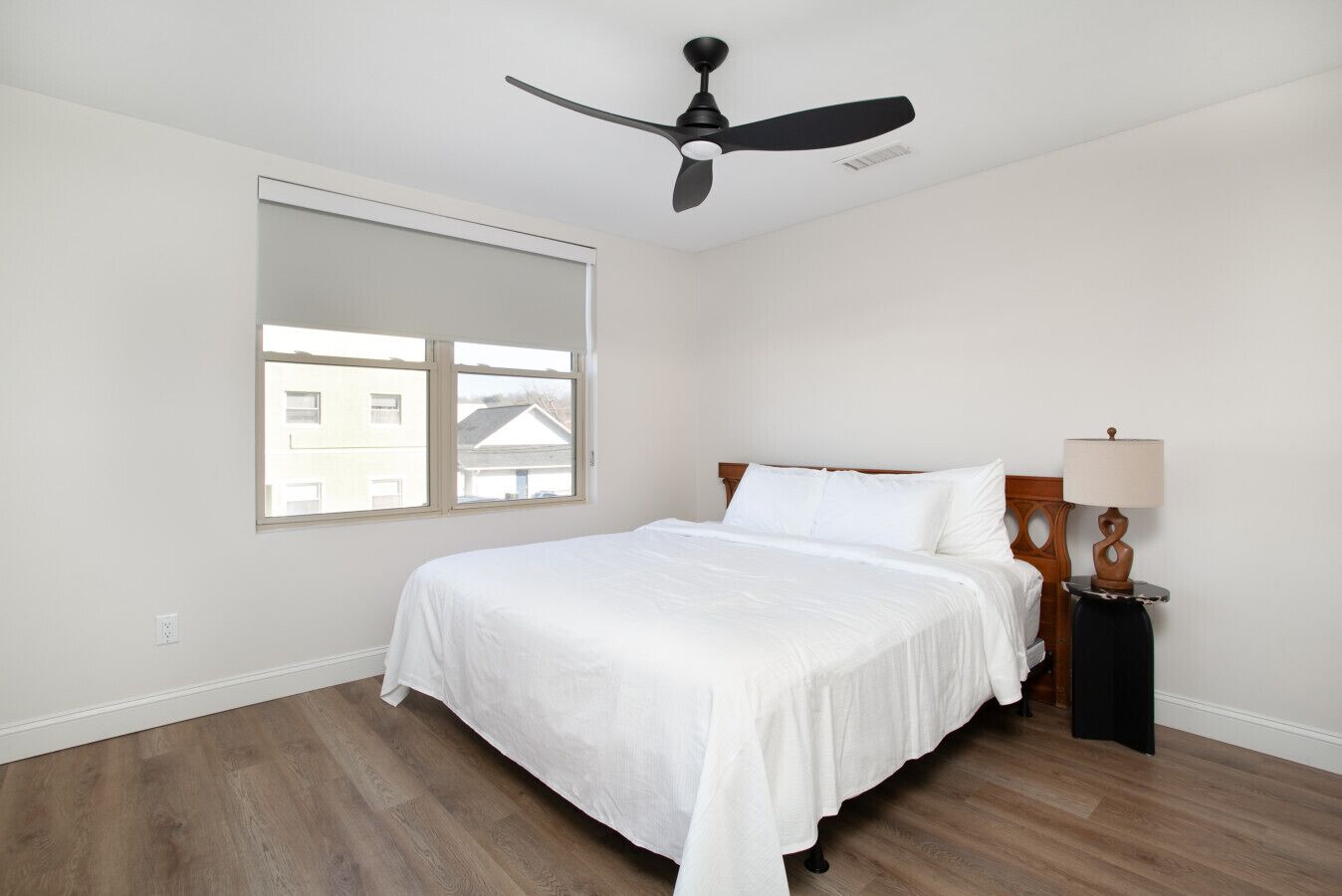 Un dormitorio con cama, ventilador de techo, ventana y mesita de noche con lámpara.
