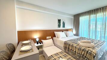 A hotel room with two beds, a small desk with a lamp, and a dining area with a table set for two.