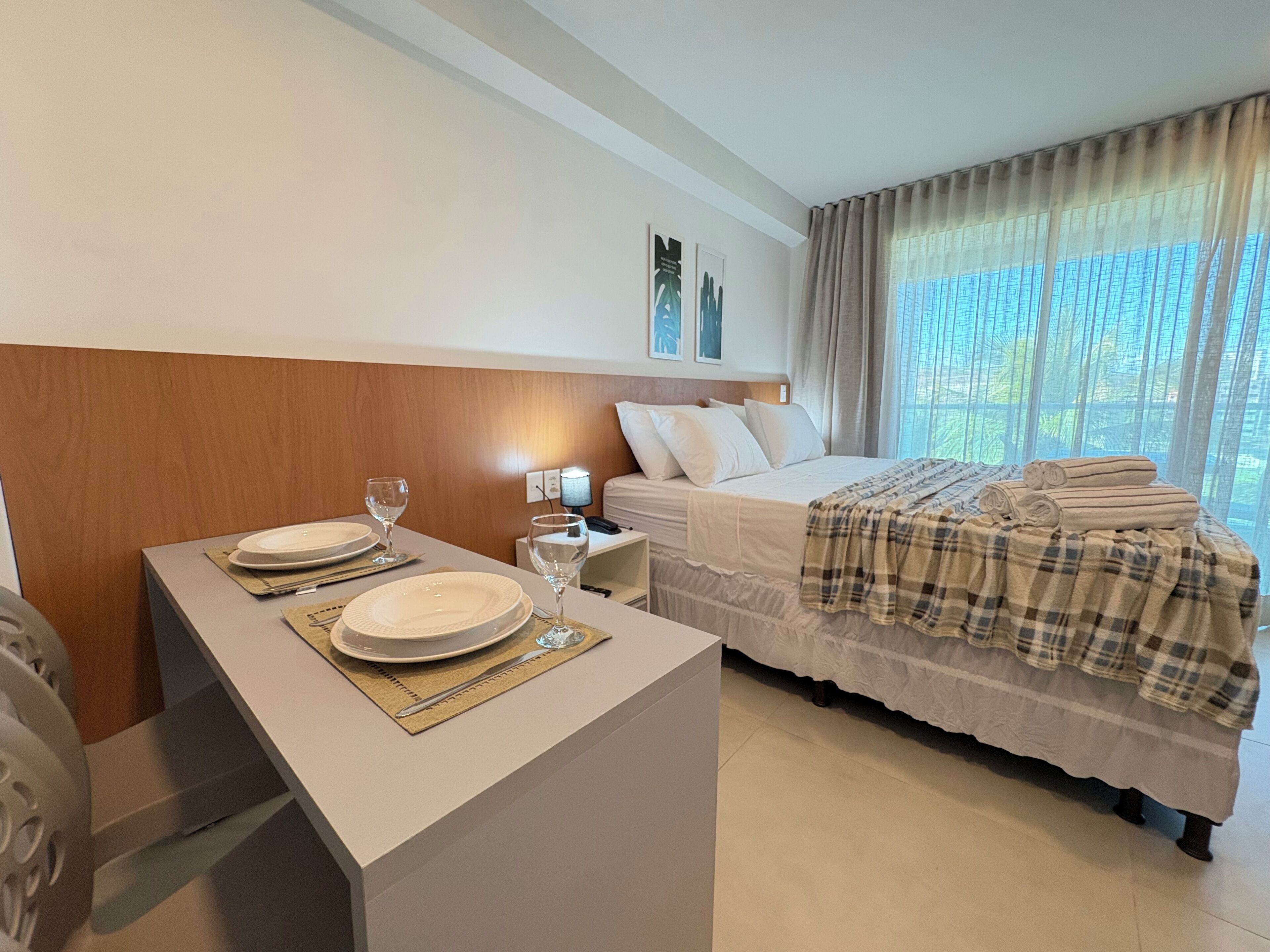 Een hotelkamer met een bed, een nachtkastje met een lamp en een raam met gordijnen.