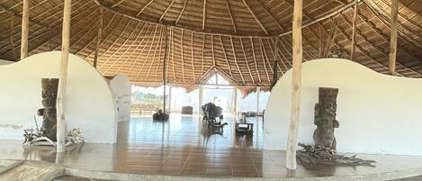 Un interior espacioso con un techo alto de paja, piso de baldosas y dos grandes esculturas de piedra.