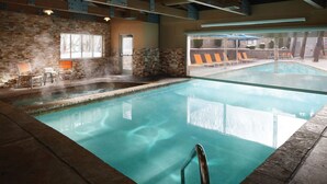 Une piscine intérieure à l’eau claire, avec des murs en pierre et des chaises longues.