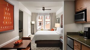 Une chambre d’hôtel avec un lit, un bureau sur lequel se trouve un panier de fruits, un four à micro-ondes, une machine à café et une vue sur la ville.