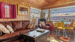 A cozy cabin interior with a leather couch, a vintage trunk, and a dining area with yellow chairs. - Romantic, Updated 1940's Cabin/ Pet Friendly | Waterfront  | Fire Pit | Kayaks (Tahuya)