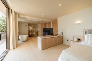 Una habitación de hotel moderna con una cama grande, un televisor, una tocador de madera y un ventanal amplio.