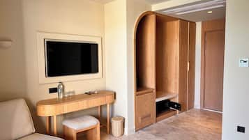 A modern room with a flat-screen TV mounted on the wall, a wooden vanity with a sink, a bench, and a wardrobe with a curved design.