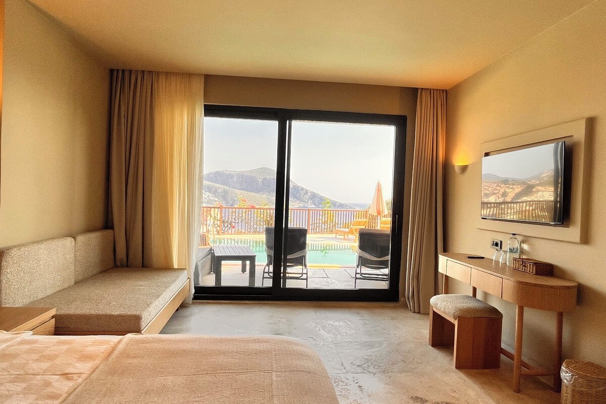 A hotel room with a bed, a desk, a chair, a television, and a view of a pool and mountains.