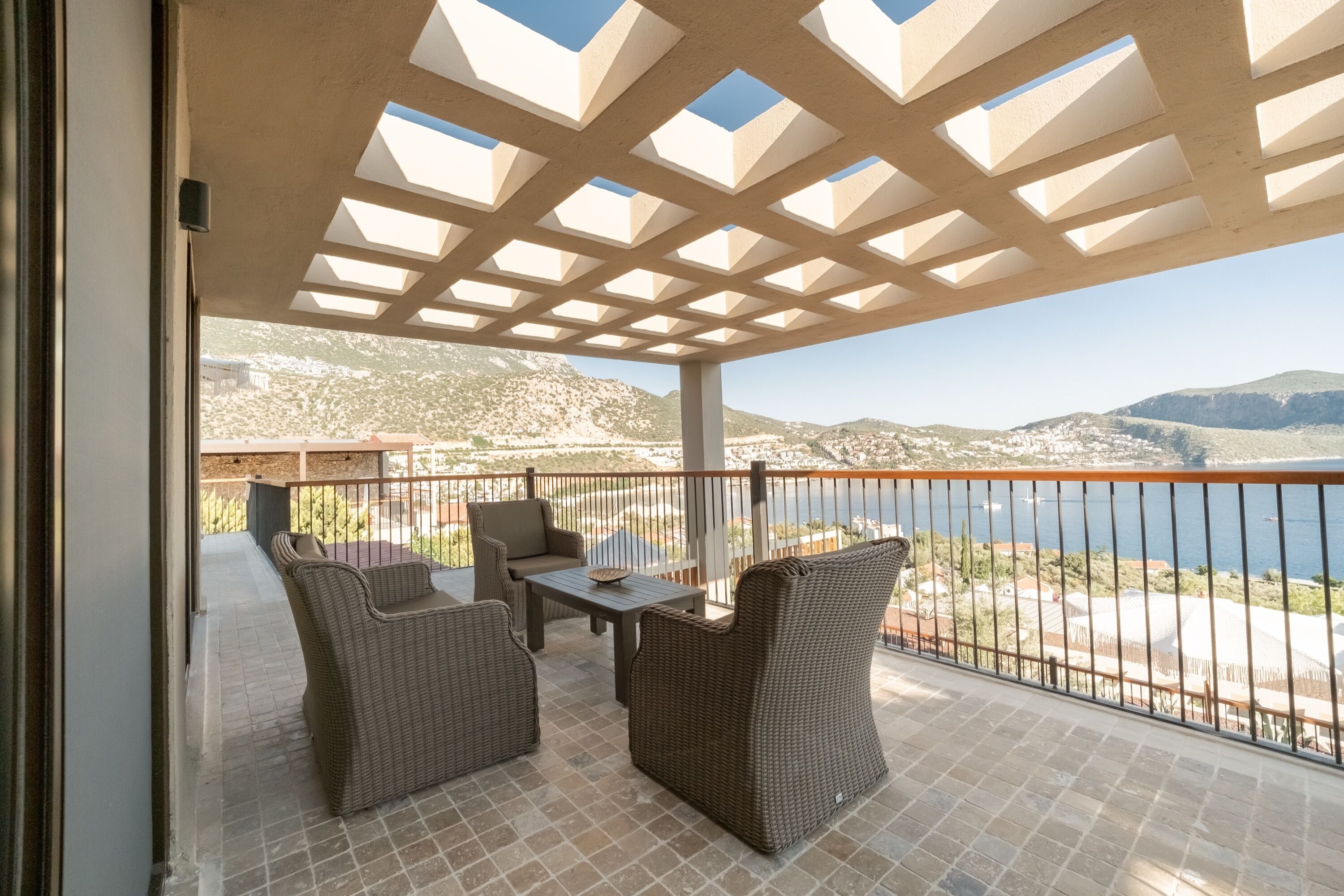 An outdoor patio with wicker furniture, a table, and a view of a coastal landscape.