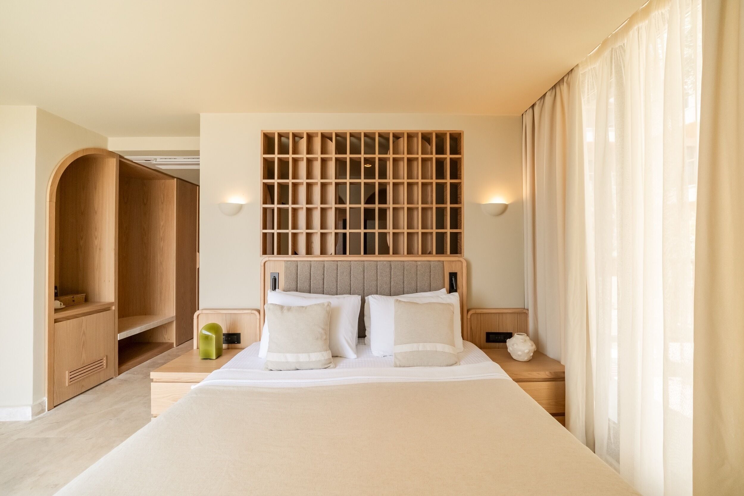 A hotel room with a large bed, wooden headboard, bedside tables, and a wardrobe.