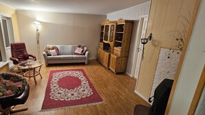 Un salon chaleureux avec un fauteuil en cuir, un canapé gris, un meuble en bois et un tapis rouge à motifs floraux.