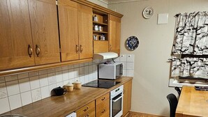 Une cuisine avec des meubles de rangement en bois, un lave-vaisselle, un four à micro-ondes et une cuisinière. Il y a un tapis sur le sol et une table à manger avec des chaises.
