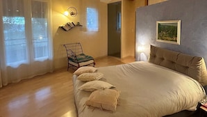 Une chambre avec un grand lit, des poutres en bois, une chaise et une fenêtre avec des rideaux.