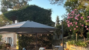 Un espace extérieur aménagé en terrasse, doté d’un coin salon couvert, d’un sol en pierre et offrant une vue sur des arbres et une montagne en arrière-plan.