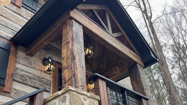 Une cabane rustique en rondins de bois, avec des fondations en pierre, des poutres apparentes et une rambarde en métal.