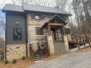A log cabin with a stone foundation, a wooden front porch, and a metal roof. - Antique log cabin with waterfall and 360 degree views of beauty! (Albertville)