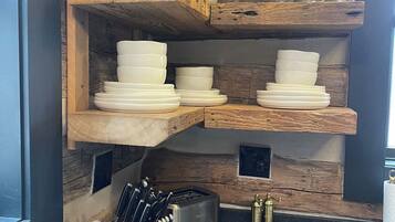A kitchen with wooden shelves holding plates and glasses, a toaster, and a knife block.