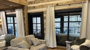 Un salon chaleureux avec un canapé gris, une petite table ronde et une grande fenêtre avec des rideaux.