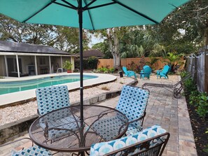 A backyard with a swimming pool, patio furniture, and a covered seating area.
