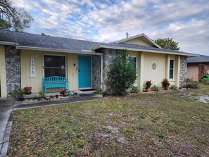 A two-story house with a stone facade, a blue door, and a front porch with a blue bench.