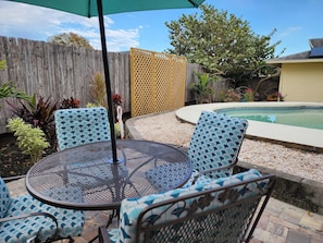 A patio with a round metal table and four chairs, a small pool, and a wooden fence.