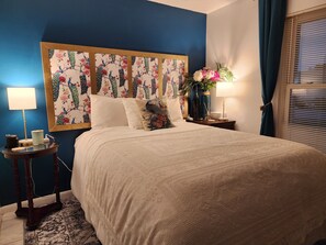 A neatly made bed with a floral headboard, a bedside table with a lamp, and a vase with flowers.