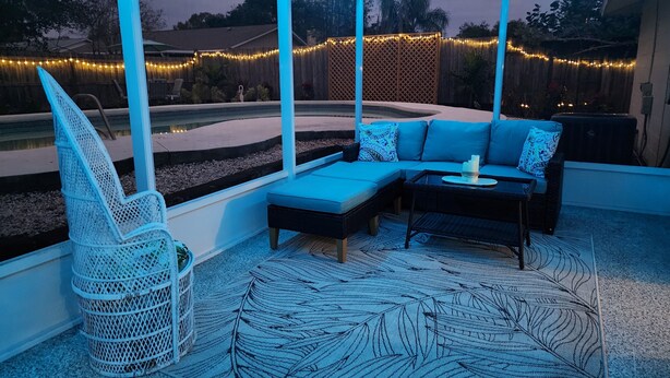 A covered outdoor seating area with a blue sofa, a wicker chair, and a table with candles. - Dori's Oasis: 3-bedroom house in Cocoa with WiFi, AC & Pool (Cocoa)
