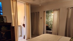 A bedroom with a bed, a wooden dresser, a television, and a view of a balcony with curtains. - Dori's Oasis: 3-bedroom house in Cocoa with WiFi, AC & Pool (Cocoa)