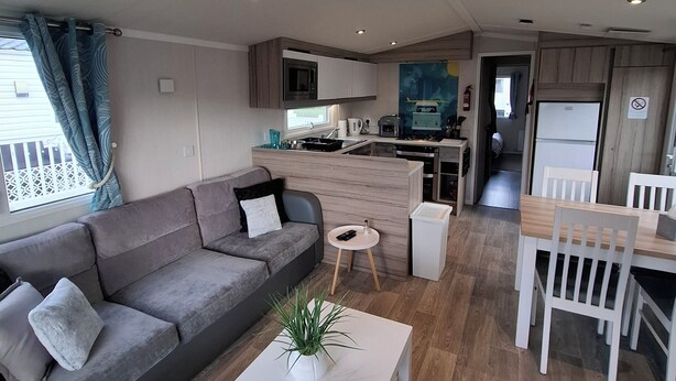 Ein modernes Wohnzimmer mit einem grauen Sofa, einem weißen Couchtisch und einem Essbereich mit einem Holztisch und weißen Stühlen.