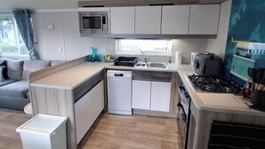 Eine moderne Küche mit integriertem Mikrowellenherd, Spüle und Herd. Ein Geschirrspüler und eine kleine Arbeitsfläche sind vorhanden. Der Boden ist aus Holz und die Schränke sind weiß.