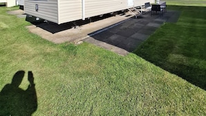 Ein Mobilheim mit einer Terrassenfläche, einer kleinen Veranda und einem Schild, das Tierhaltung erlaubt.