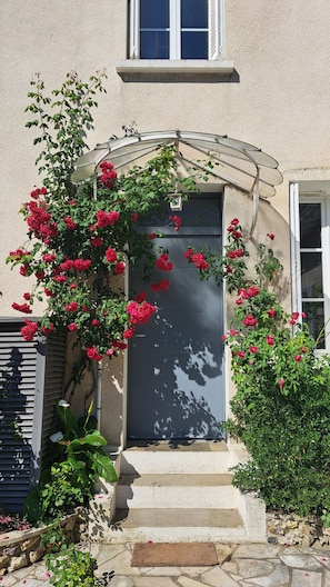 Una casa con una puerta oscura, un pequeño porche y un jardín con flores rojas.
