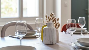 Una mesa de comedor decorada con platos blancos, copas de vino transparentes y un florero de mármol con plumas de pampa.