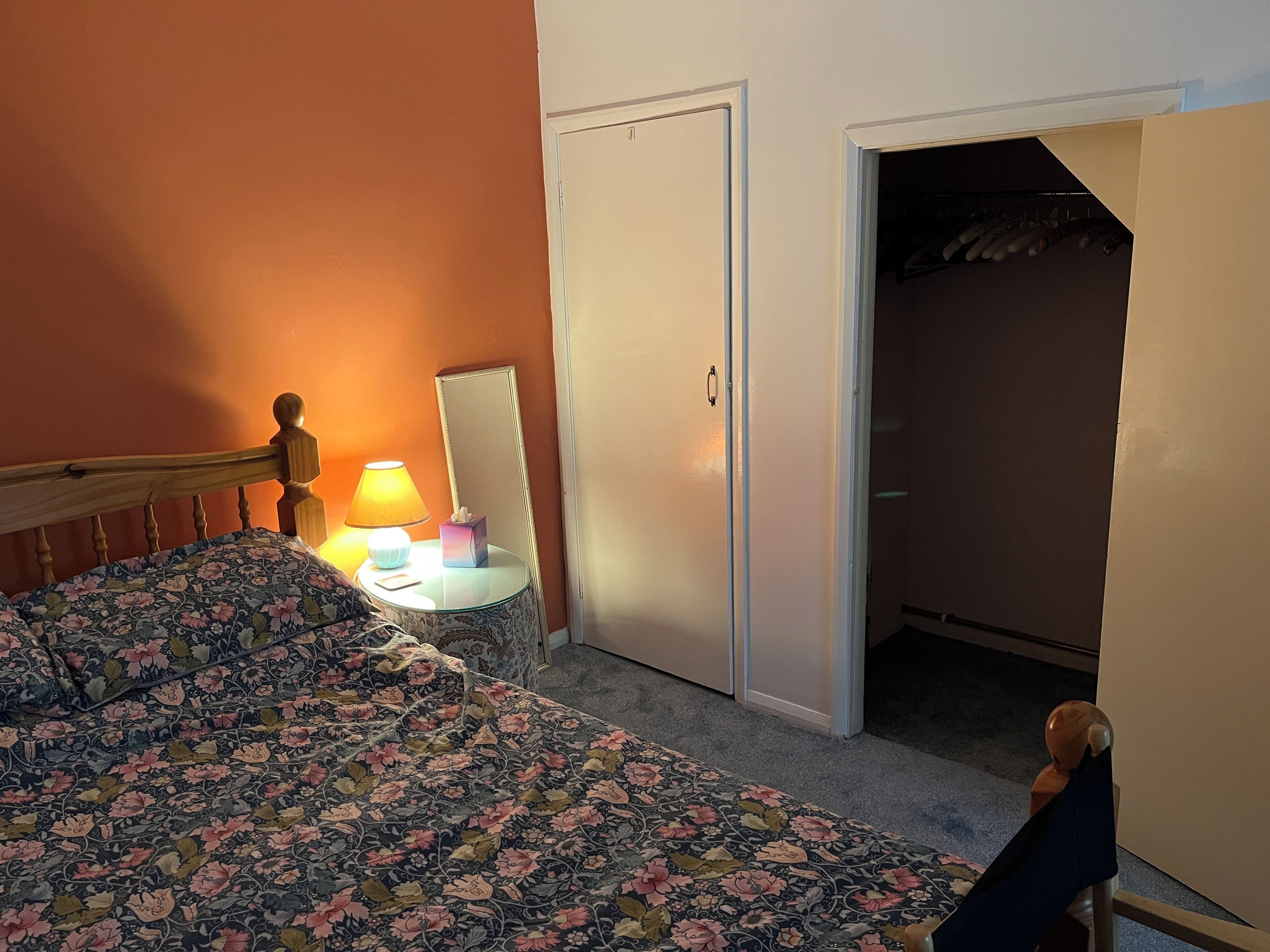 Una camera da letto con un letto, un comodino con una lampada, uno specchio e un armadio.